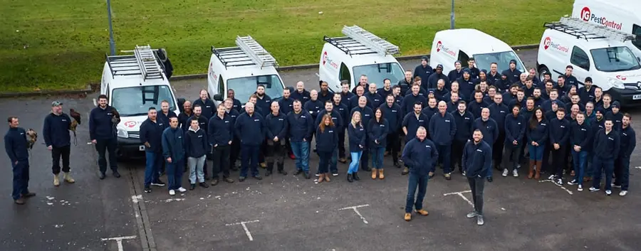 The JG Pest Control team standing in front of a row of JG vans