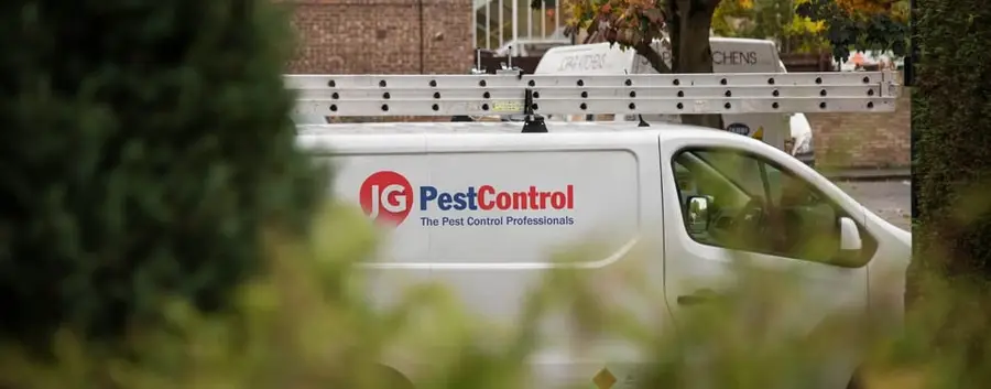 A white JG Pest Control van seen past a garden hedge